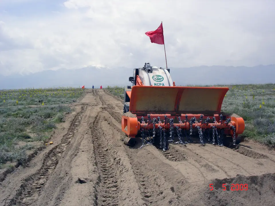 A mechanical demining flail marked with a red flag works along a track through scrubland.
