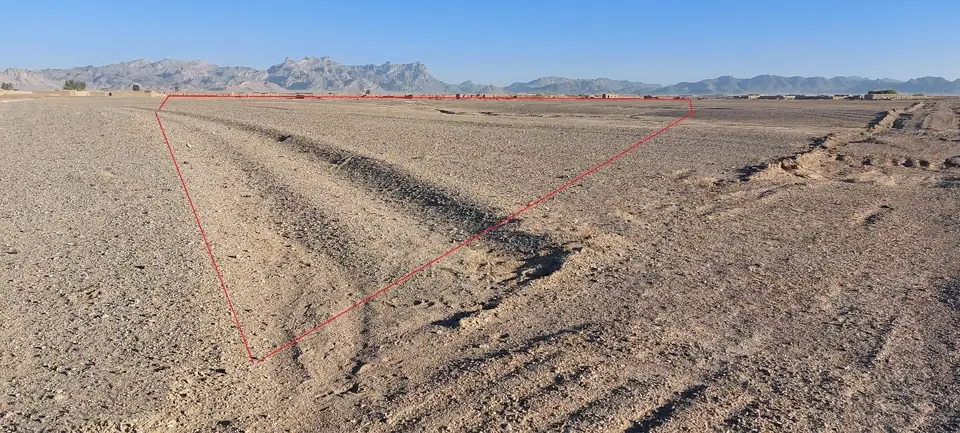 Flat, bare brown ground under a pale sky, with the outline of the hazardous area drawn over it in red.