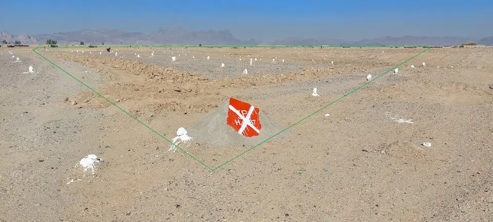 The same bare ground after clearance, dotted with small white markers, with a red-and-white sign in the centre.