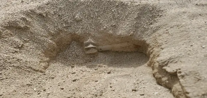A partly excavated hole in sandy soil, with the base of an artillery shell exposed at the bottom.