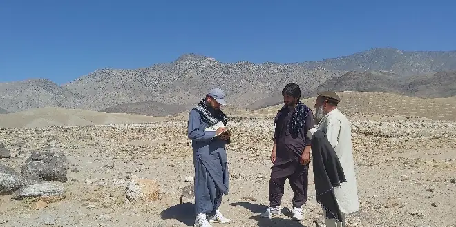 An MCPA surveyor with a clipboard talks with two local men on open ground below a mountain ridge.