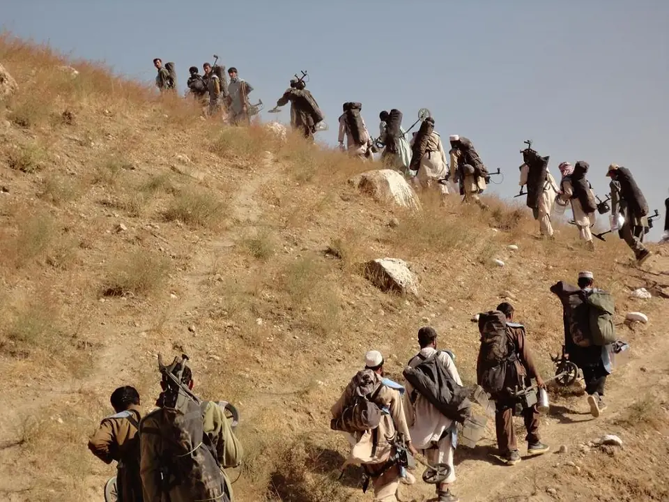 A long line of deminers carrying their equipment walks up a dry hillside towards a work site.