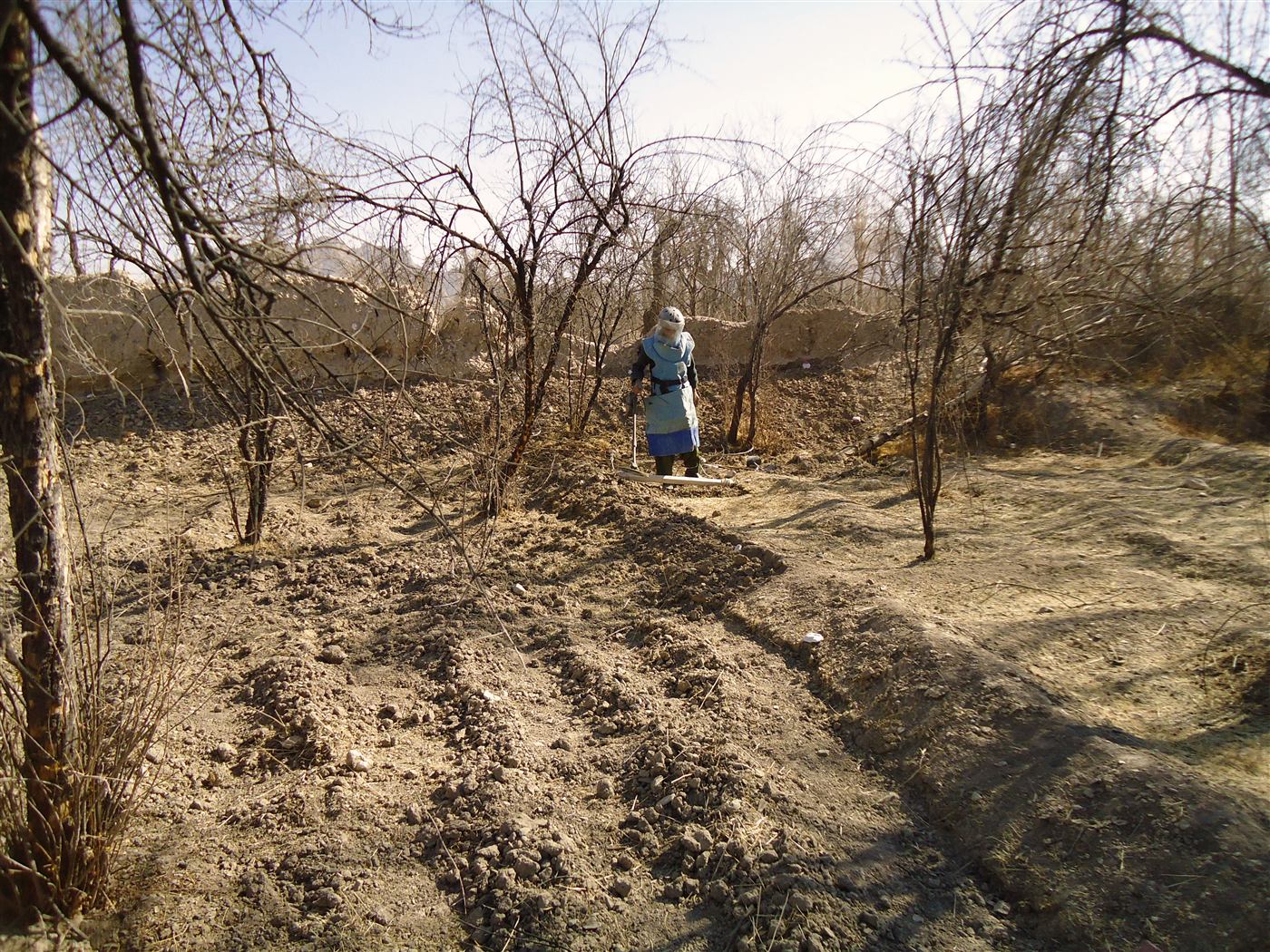 An MCPA deminer in protective equipment searching the ground with a metal detector