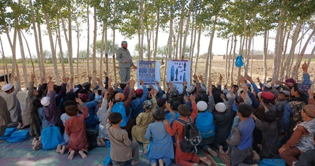 Boys raising their hands to answer during an MCPA risk education session held outdoors beside a village mosque